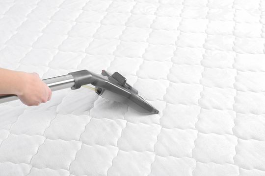 Professional cleaning a mattress with steam equipment in a bright bedroom
