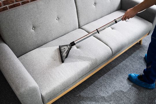 Technician steam-cleaning a fabric sofa in a modern home